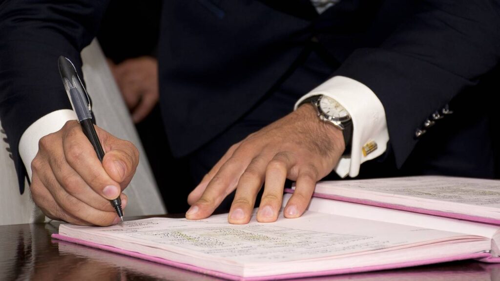 A man wearing a wrist watch signing a document