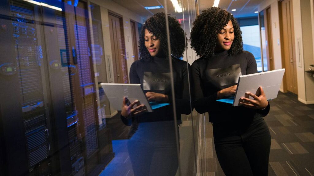 A black woman using a laptop next to a large server computer