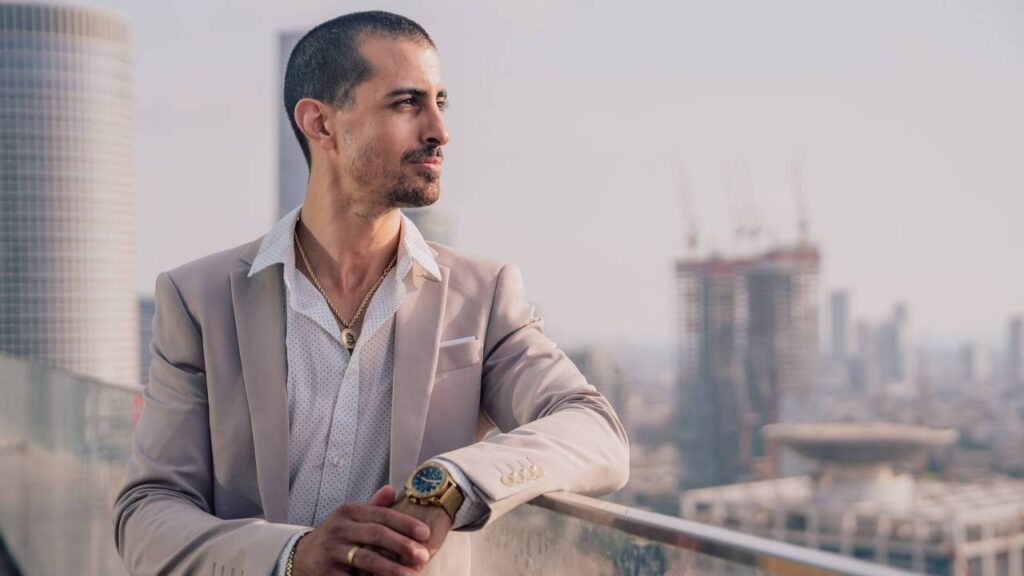 A businessman wearing golden jewelry looking at the city from a terrace